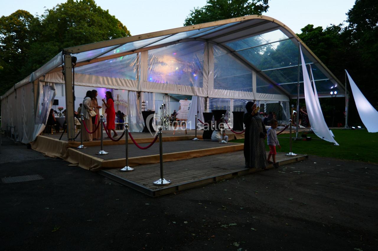 Tente transparente éclairée en soirée, avec des invités debout et un espace extérieur aménagé.