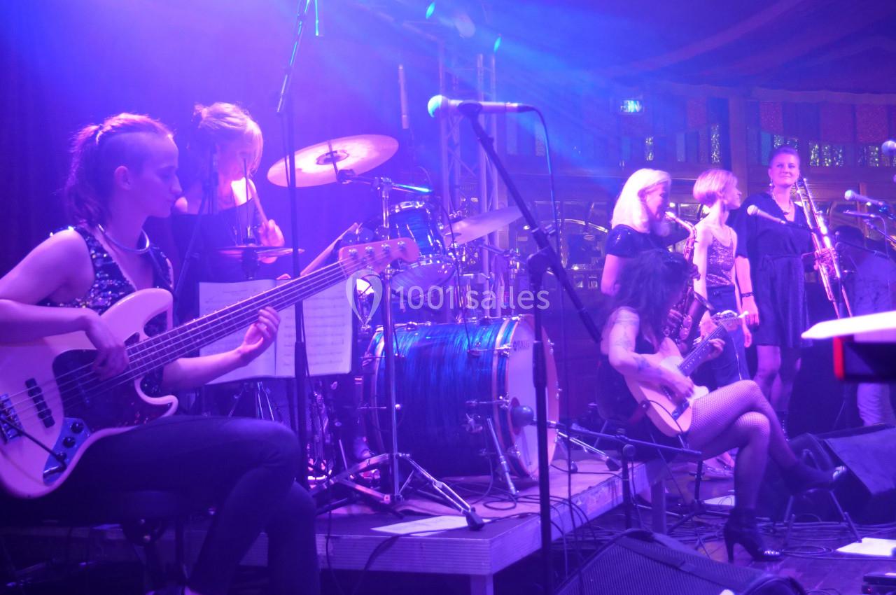Groupe de musiciens sur scène jouant différents instruments sous des lumières violettes dans une ambiance de concert.