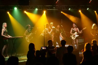 Un bus stationné de nuit devant un bâtiment illuminé, avec des passants en arrière-plan.