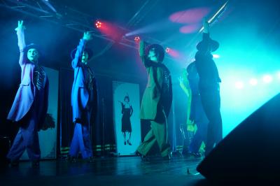 Un bus stationné de nuit devant un bâtiment illuminé, avec des passants en arrière-plan.