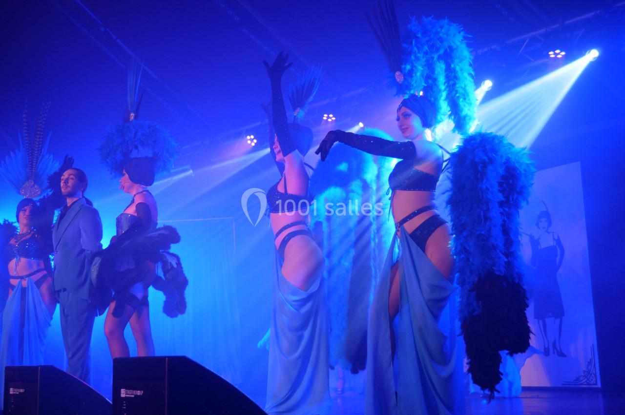 Danseurs et danseuses en costumes de cabaret bleu et noir sur une scène éclairée par des projecteurs.