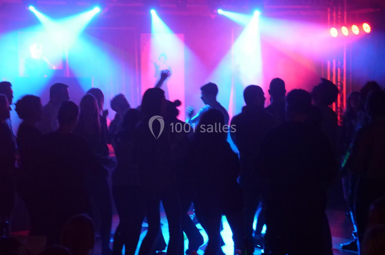Groupe de personnes dansant dans une salle sombre éclairée par des lumières colorées bleues et rouges.