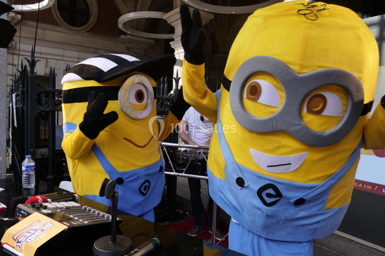 Deux mascottes jaunes déguisées en personnages de dessin animé interagissent joyeusement devant une table de mixage.