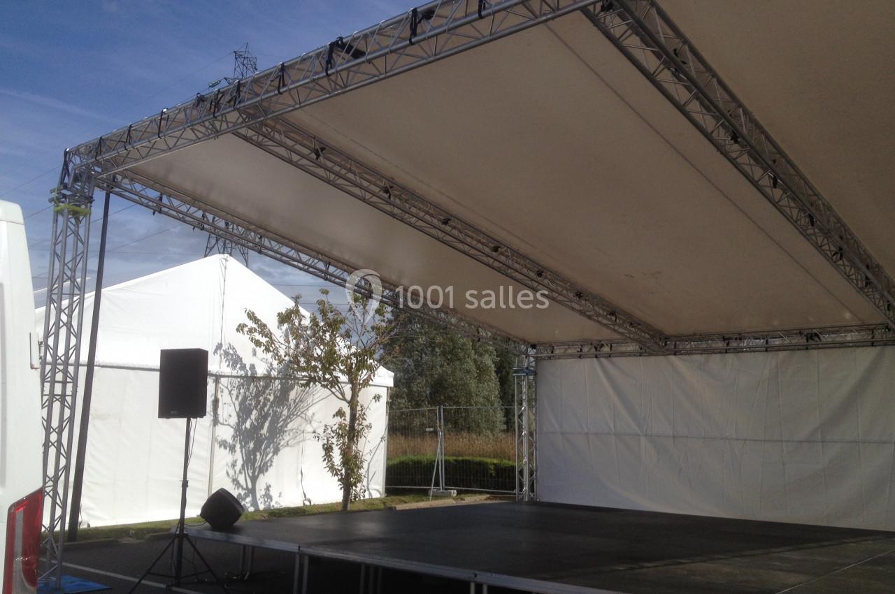 Structure de scène extérieure avec toit en toile blanche, montée sur une plateforme surélevée, en plein air.