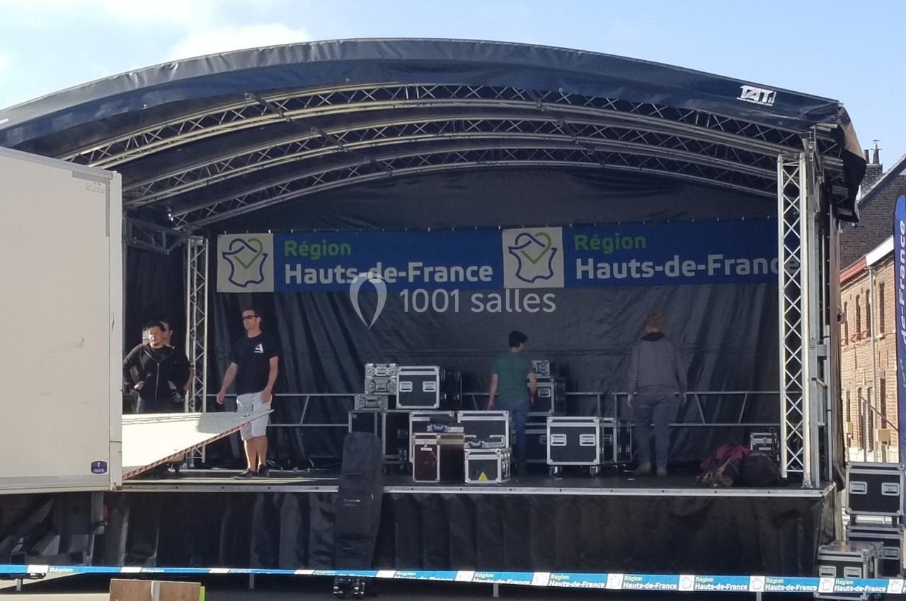 Scène extérieure en cours de montage avec des techniciens et du matériel, sous une bannière ’Région Hauts-de-France’.