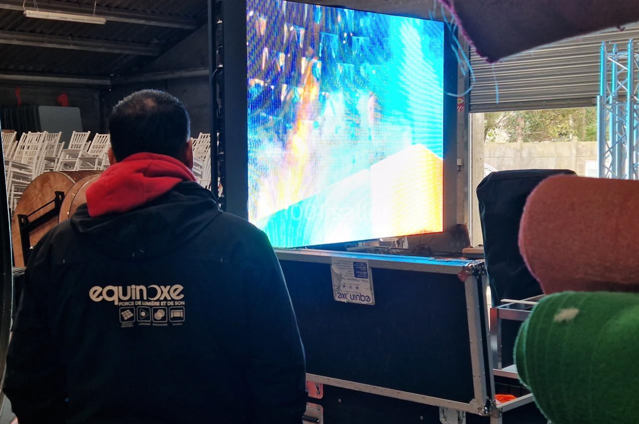 Un technicien observe un écran LED coloré installé dans un espace intérieur avec des équipements techniques autour.
