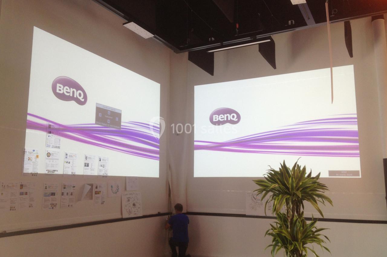 Deux écrans projetant des visuels BenQ dans une salle avec des documents affichés au mur et une plante au premier plan.