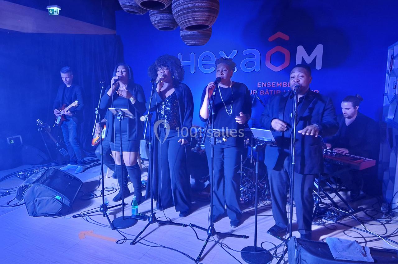 Un groupe de musiciens et chanteurs se produit sur scène dans une ambiance éclairée en bleu.