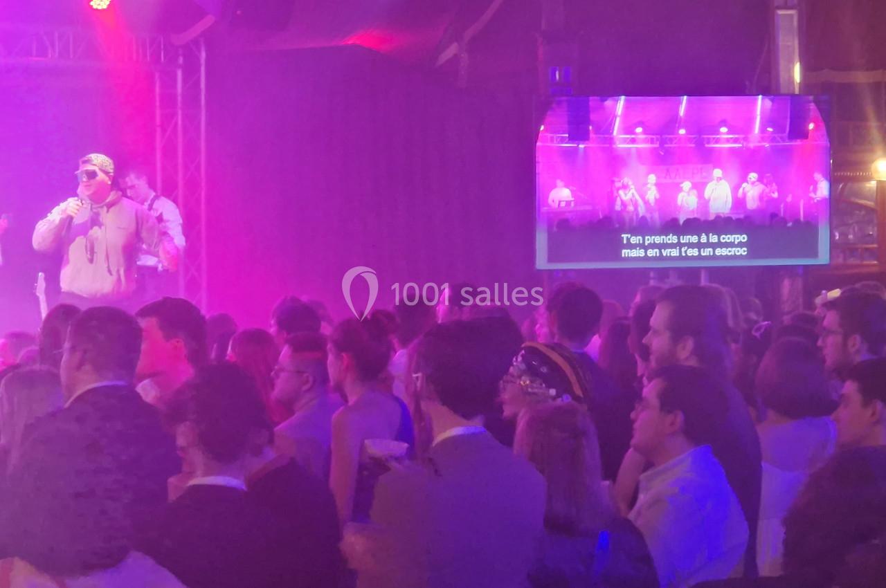 Un chanteur sur scène sous des lumières violettes, face à une foule, avec des paroles affichées sur un écran.