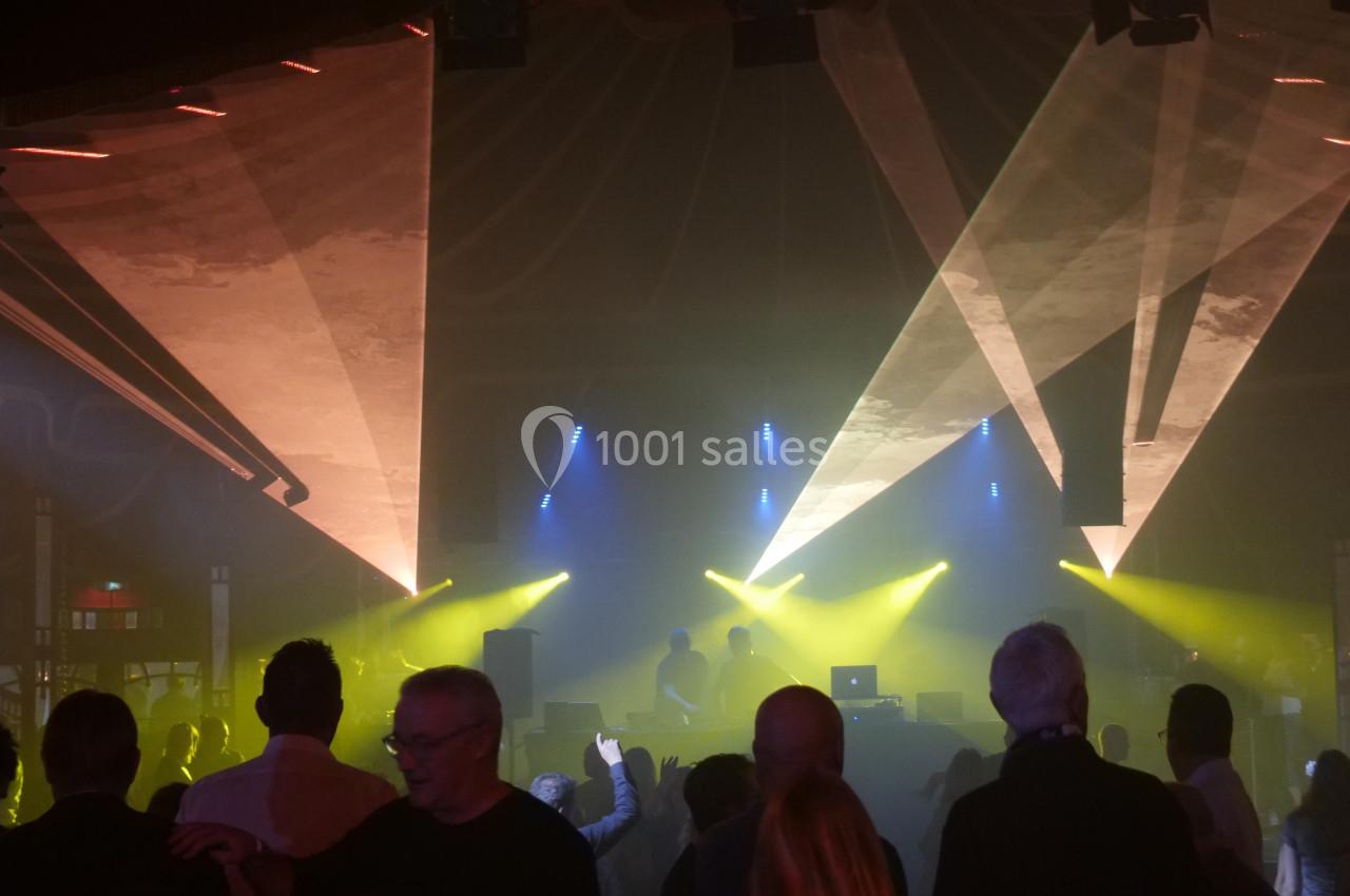 Des personnes dansent sous des jeux de lumière colorés dans une salle sombre avec des DJ sur scène.