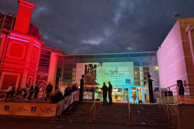 Un bus stationné de nuit devant un bâtiment illuminé, avec des passants en arrière-plan.