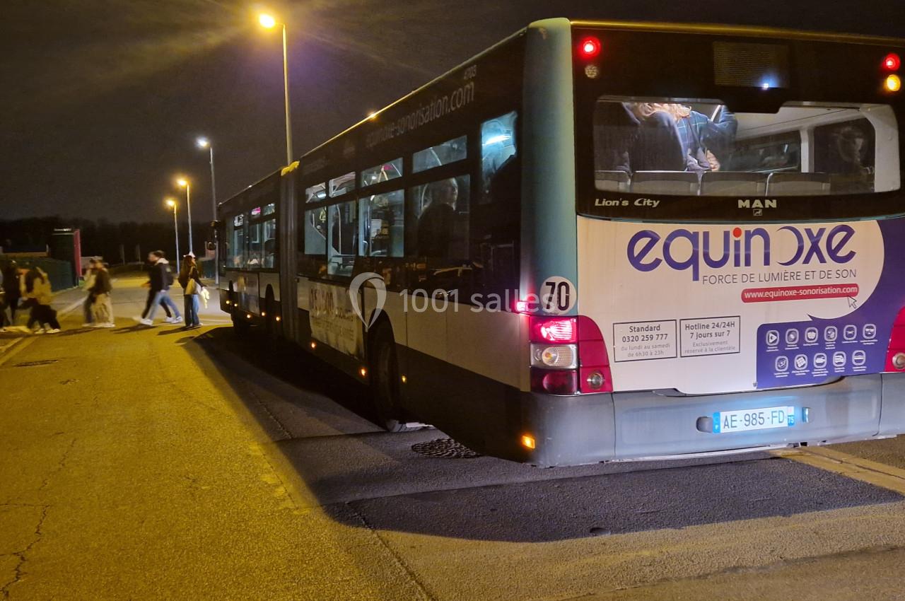 Un bus à l'arrêt de nuit, des passagers montent ou descendent sous un éclairage public.