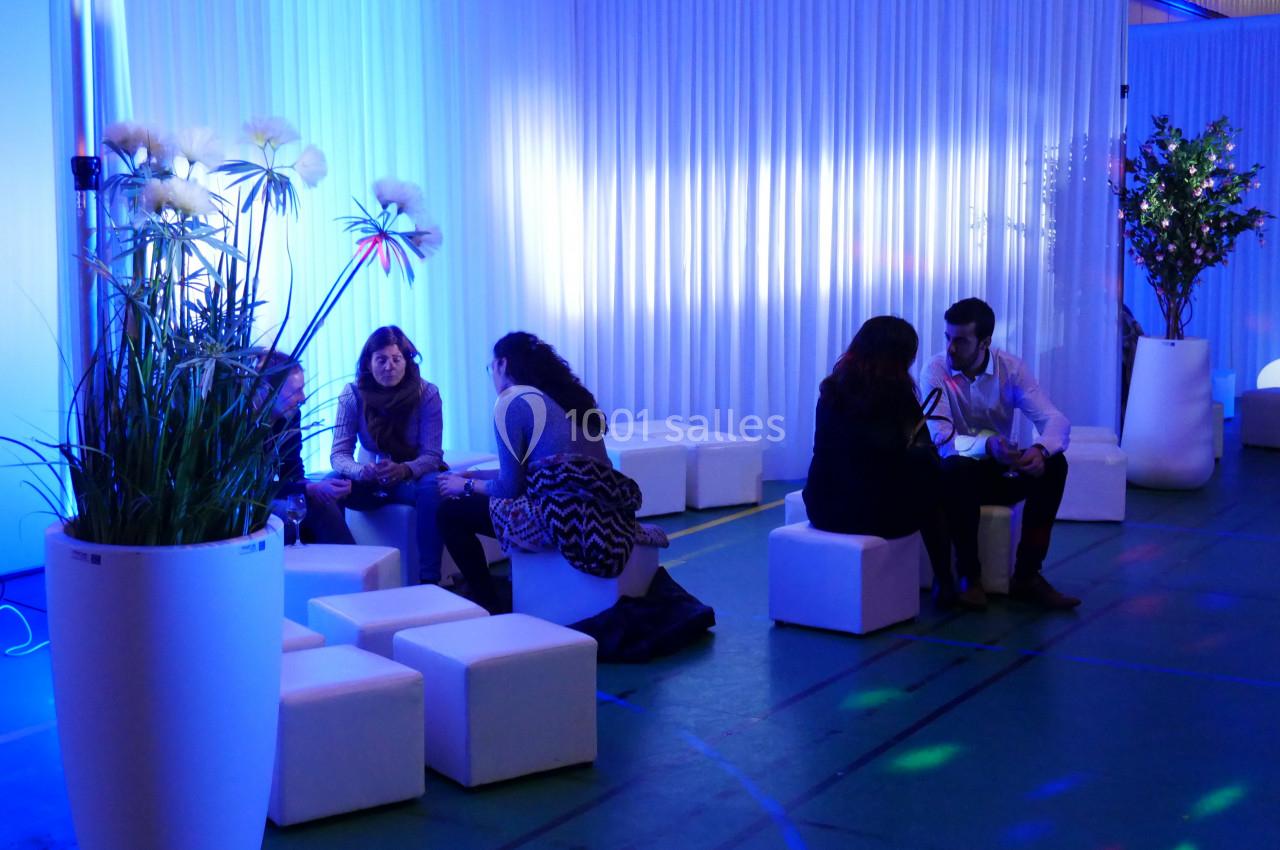 Des personnes assises sur des cubes blancs discutent dans un espace lumineux avec des plantes et des éclairages colorés.
