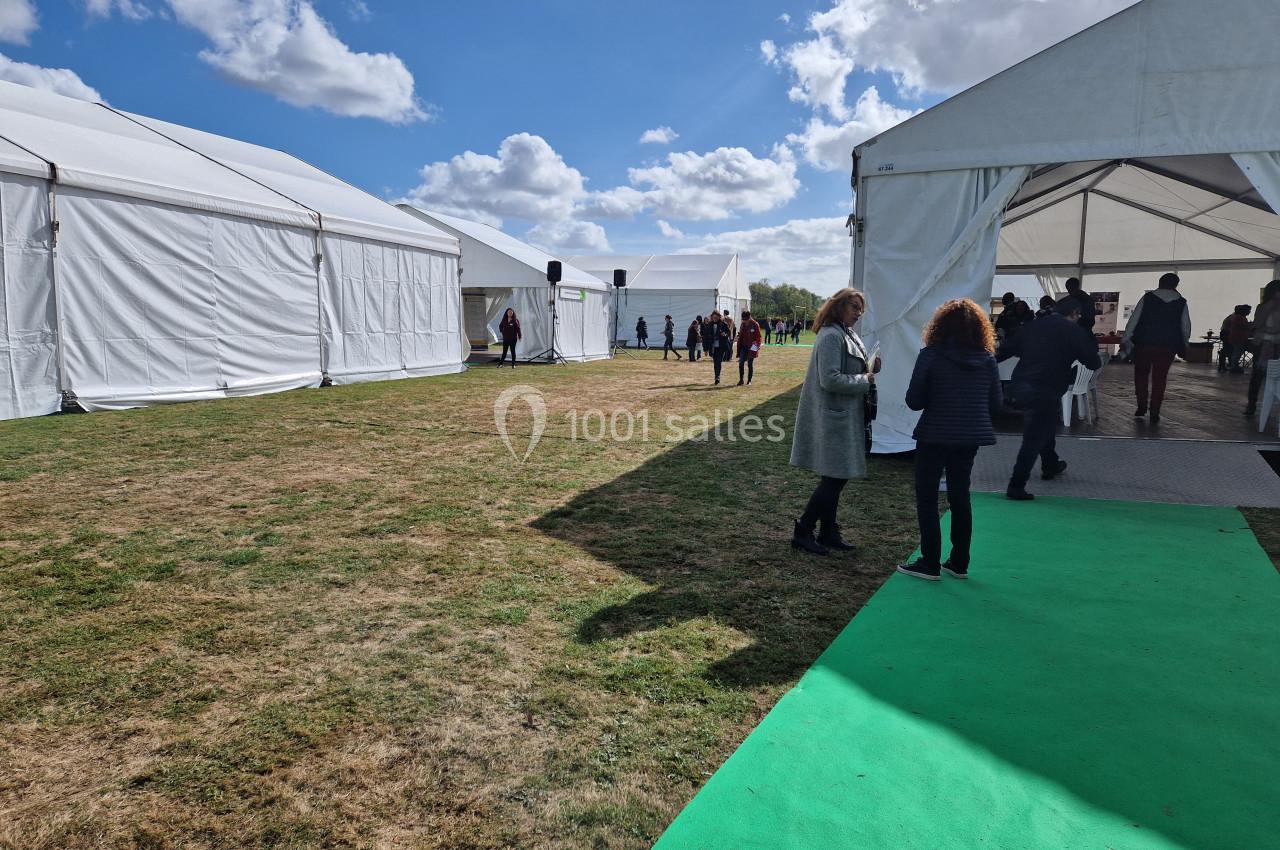Des personnes discutent près de tentes blanches installées sur une pelouse sous un ciel partiellement nuageux.