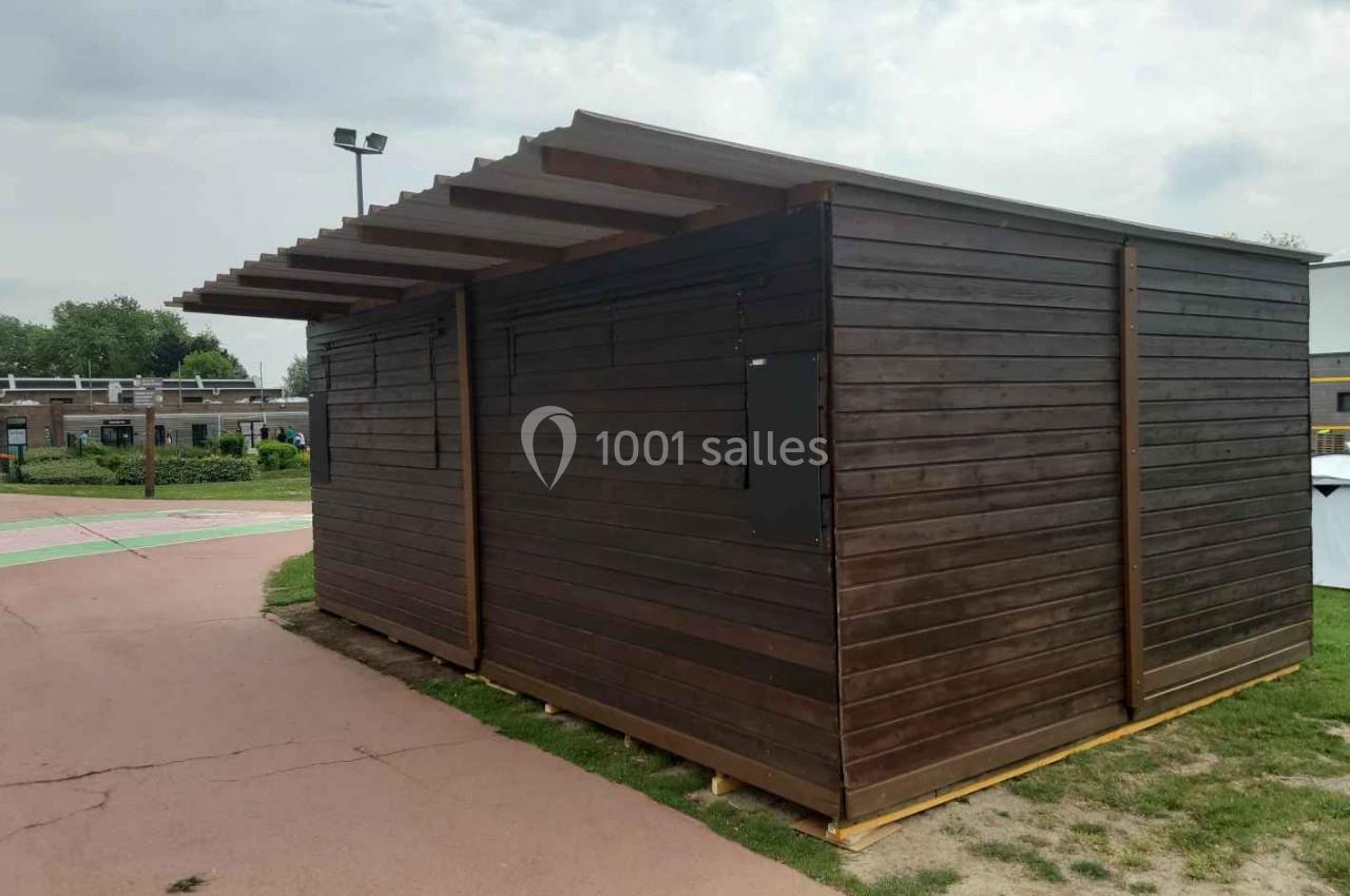 Abri en bois sombre avec toit incliné, situé sur un chemin pavé dans un espace extérieur dégagé.