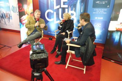 Un bus stationné de nuit devant un bâtiment illuminé, avec des passants en arrière-plan.