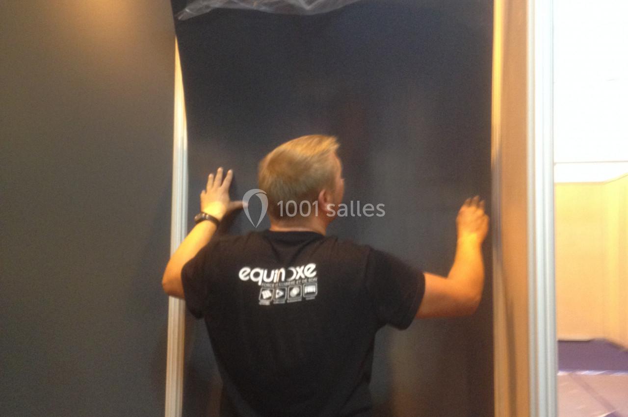 Un homme installe un panneau noir sur une structure lors d'un montage d'exposition en intérieur.