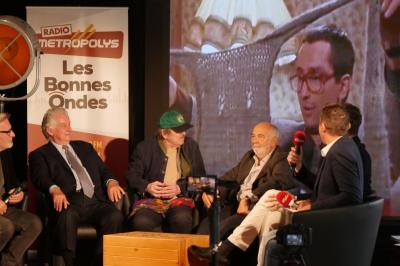 Un bus stationné de nuit devant un bâtiment illuminé, avec des passants en arrière-plan.