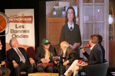Un bus stationné de nuit devant un bâtiment illuminé, avec des passants en arrière-plan.