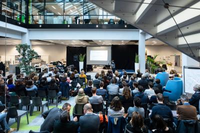 Un bus stationné de nuit devant un bâtiment illuminé, avec des passants en arrière-plan.