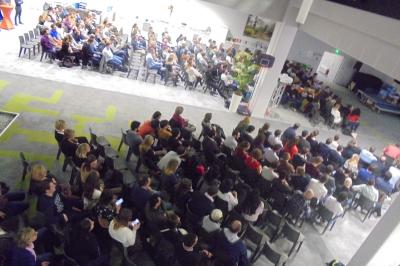 Un bus stationné de nuit devant un bâtiment illuminé, avec des passants en arrière-plan.