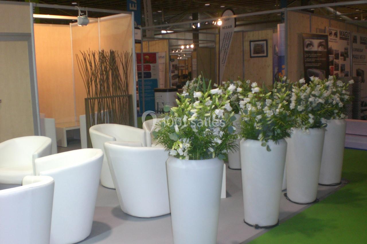 Des fauteuils blancs entourent des plantes en pots dans un espace d'exposition au sol gris et vert.