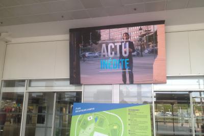 Un bus stationné de nuit devant un bâtiment illuminé, avec des passants en arrière-plan.