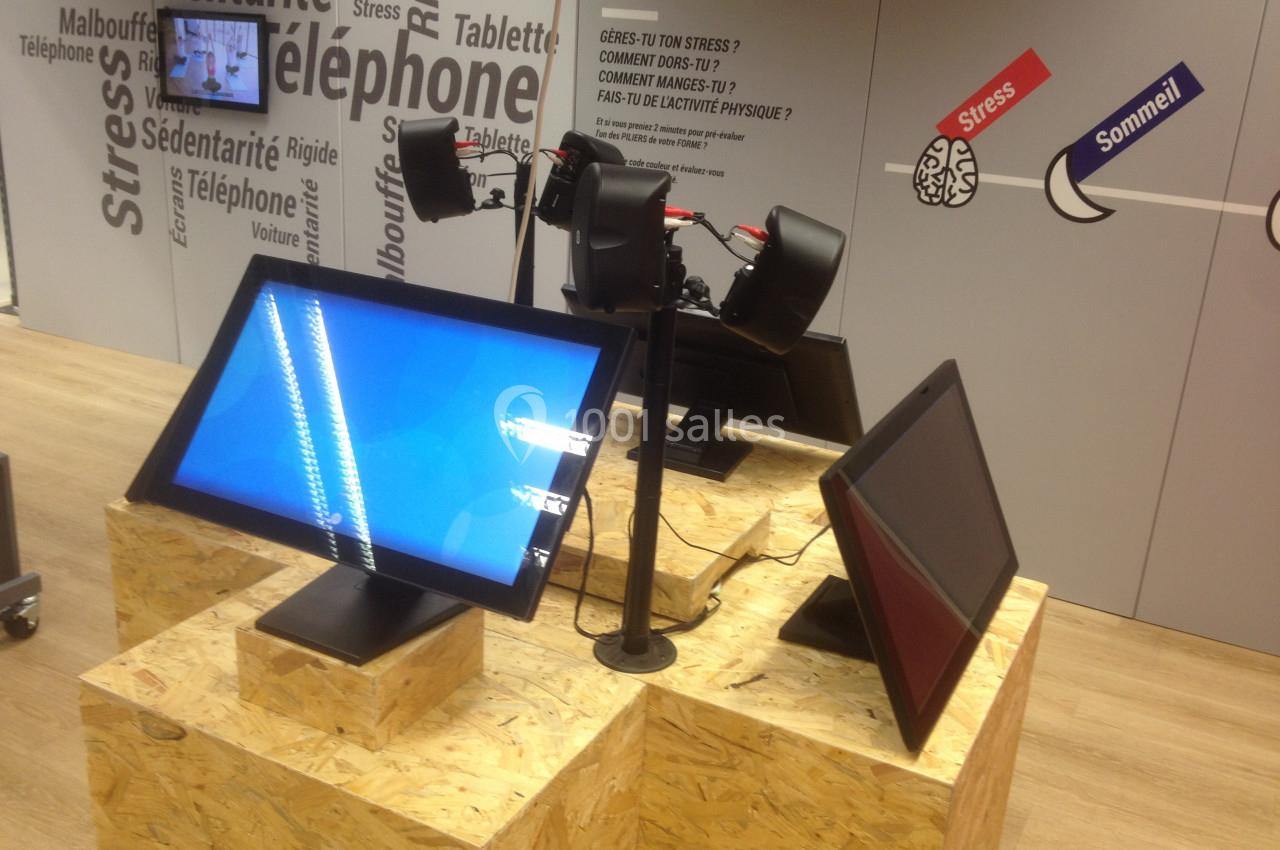 Trois écrans interactifs sur des supports en bois, exposés dans un espace avec des affiches murales éducatives.