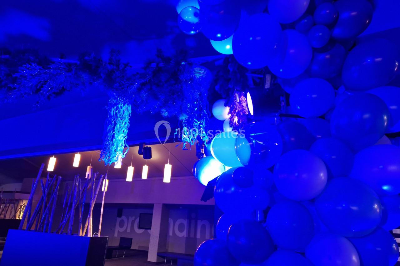 Décoration intérieure avec ballons bleus et éclairage tamisé, ornée de végétation suspendue.