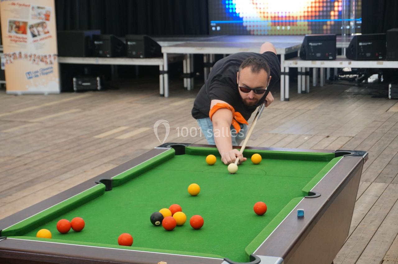 Un homme joue au billard sur une table verte dans un espace intérieur avec un sol en bois.