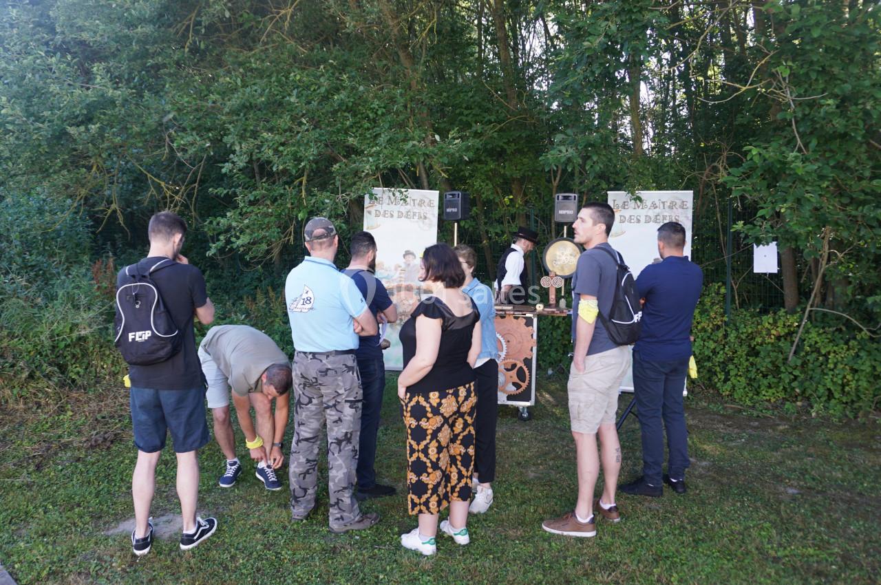 Des personnes rassemblées devant un stand en plein air dans un cadre boisé, observant une animation ou une activité.