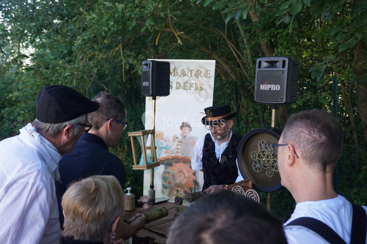 Un homme en costume anime un atelier artisanal en plein air devant un petit groupe de personnes attentives.