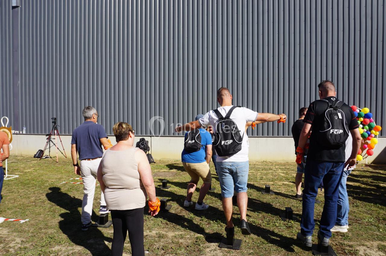 Des personnes participent à une activité en plein air devant un bâtiment gris, portant des sacs à dos noirs.