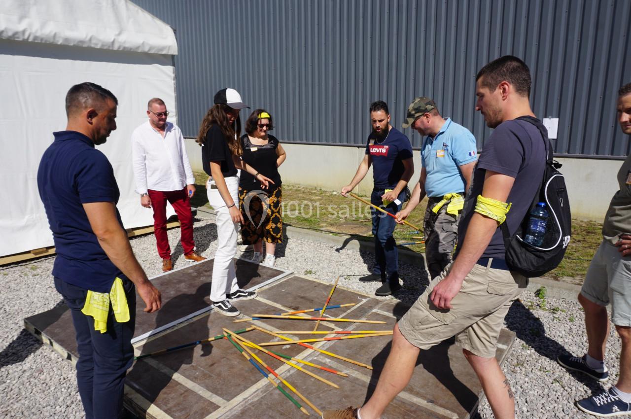 Des personnes participent à une activité en groupe autour de bâtons colorés posés sur une plateforme en extérieur.