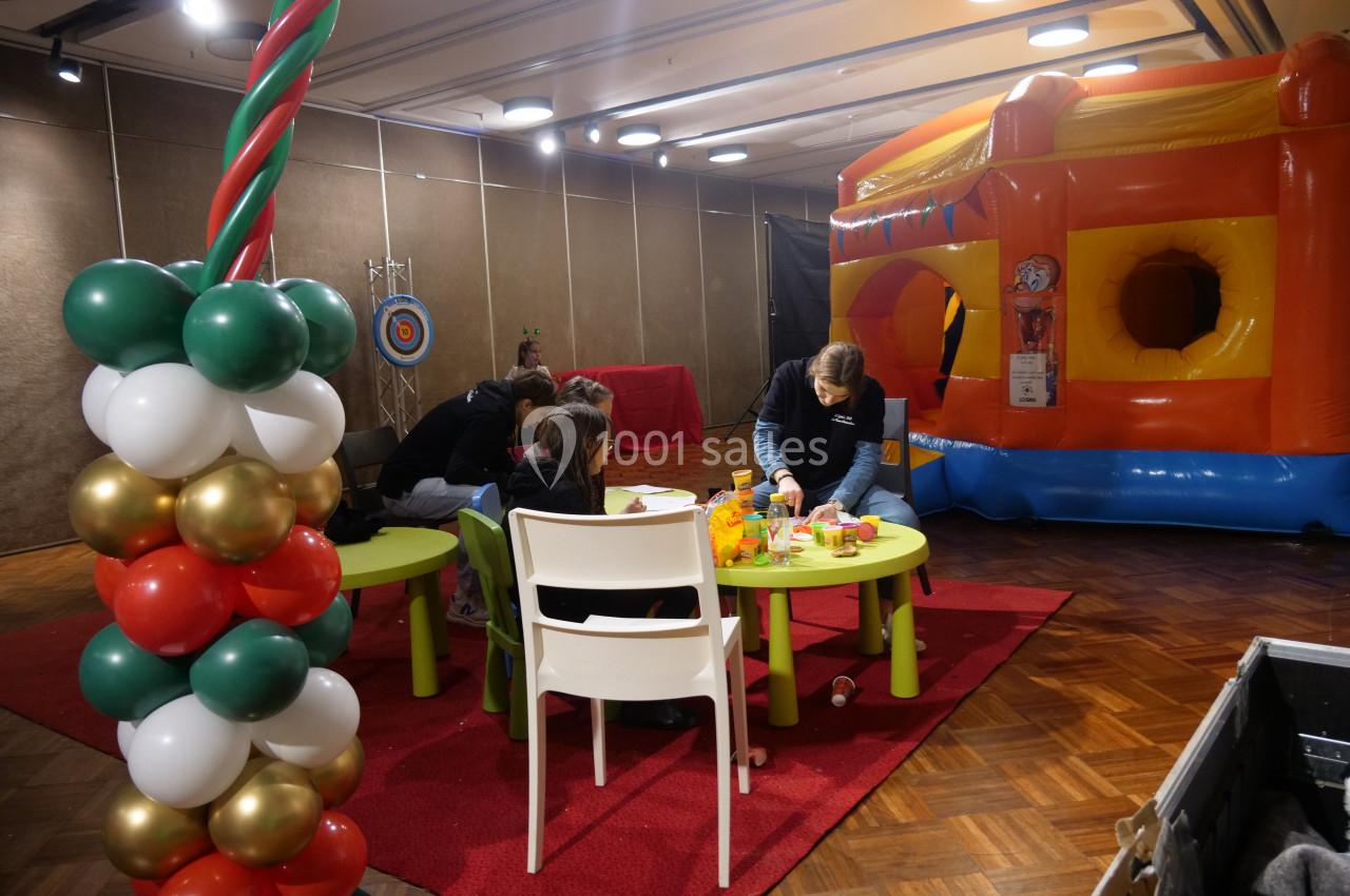 Des enfants et des adultes participent à des activités créatives près d'une structure gonflable colorée en intérieur.