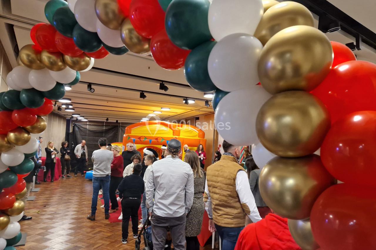 Arc de ballons colorés décorant une salle avec des personnes rassemblées près d'une structure gonflable.
