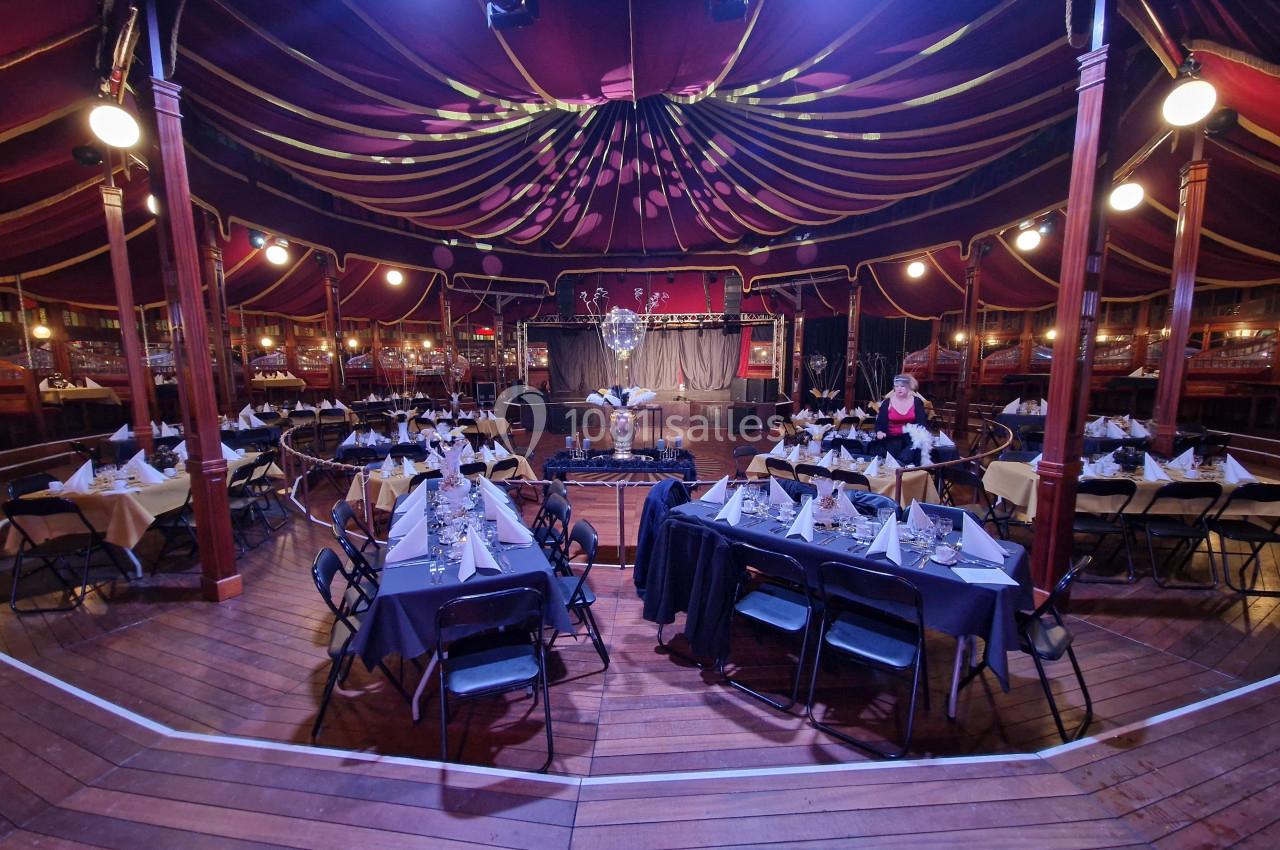 Salle de réception décorée avec des tables dressées, nappes blanches et éclairage tamisé sous une tente élégante.