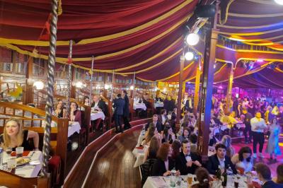 Un bus stationné de nuit devant un bâtiment illuminé, avec des passants en arrière-plan.