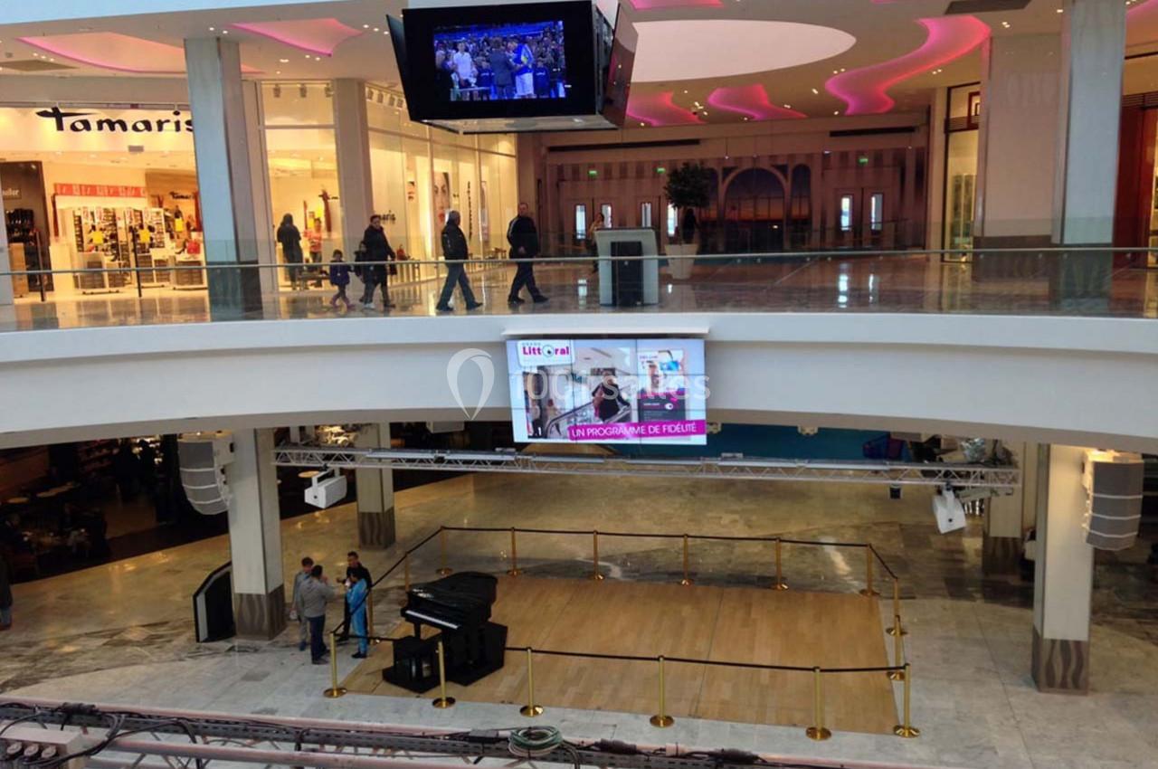 Écran géant affichant une publicité dans un centre commercial avec des passants et des boutiques en arrière-plan.