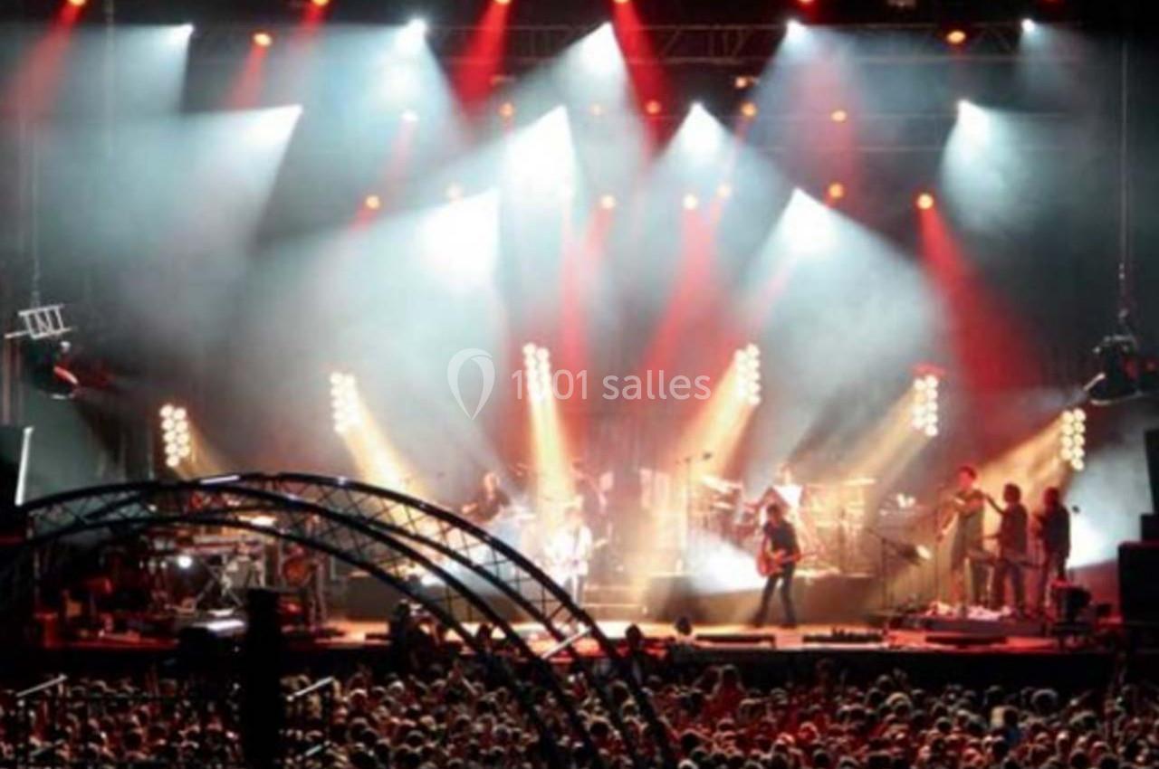 Foule rassemblée devant une scène illuminée lors d'un concert en plein air, avec des musiciens et des jeux de lumière.