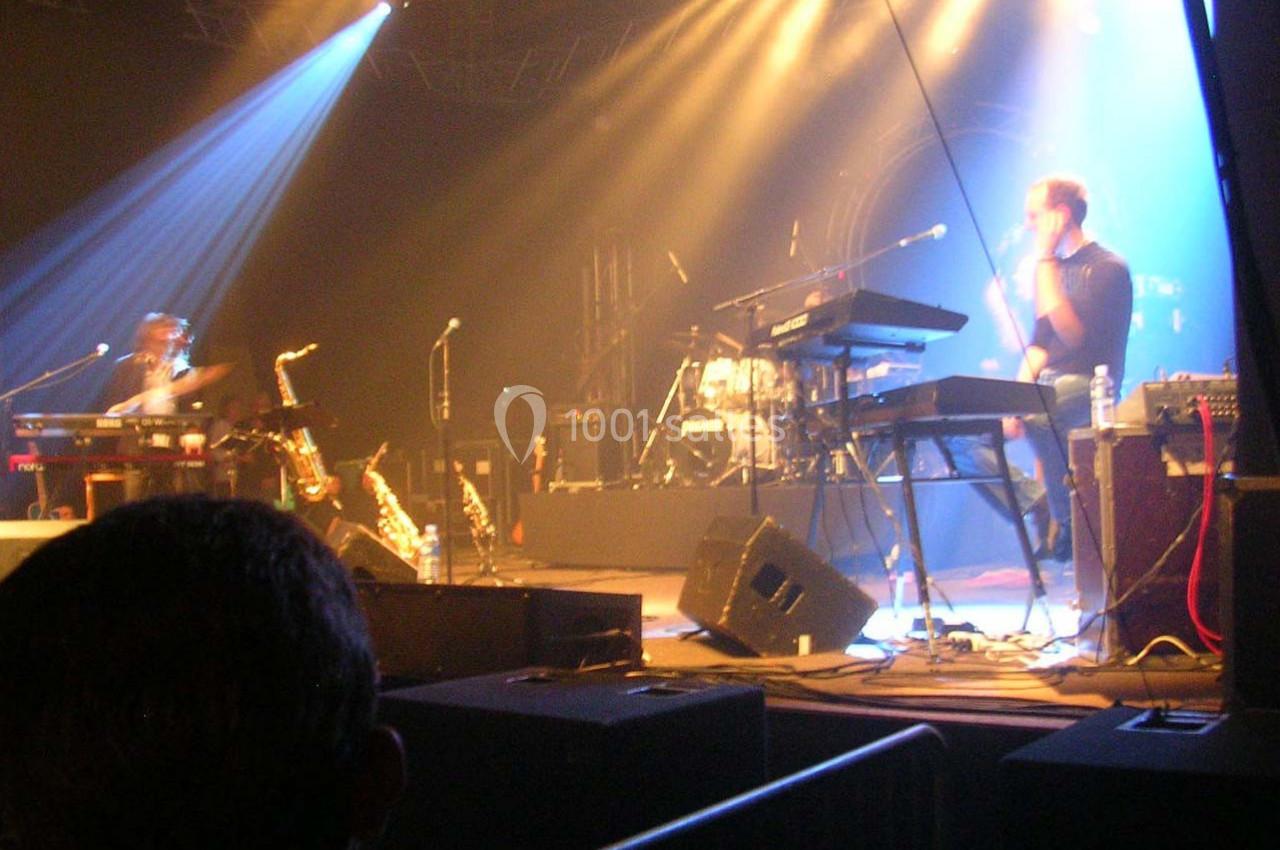 Musiciens jouant sur scène sous des éclairages colorés, entourés d'instruments et d'équipements.