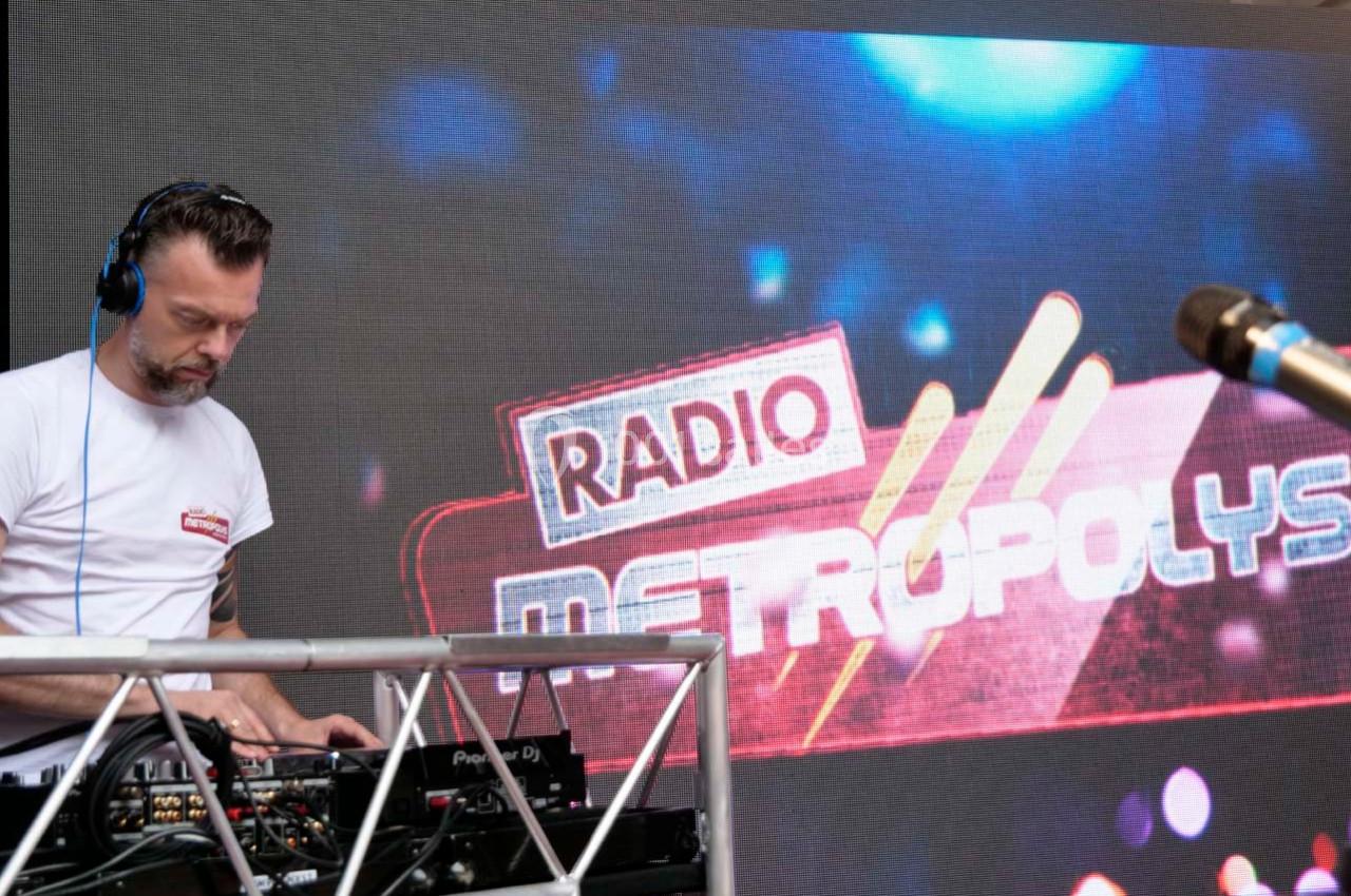 Un DJ mixe sur une console devant un écran affichant ’Radio Metropolys’ avec des lumières en arrière-plan.