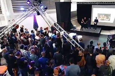 Un bus stationné de nuit devant un bâtiment illuminé, avec des passants en arrière-plan.