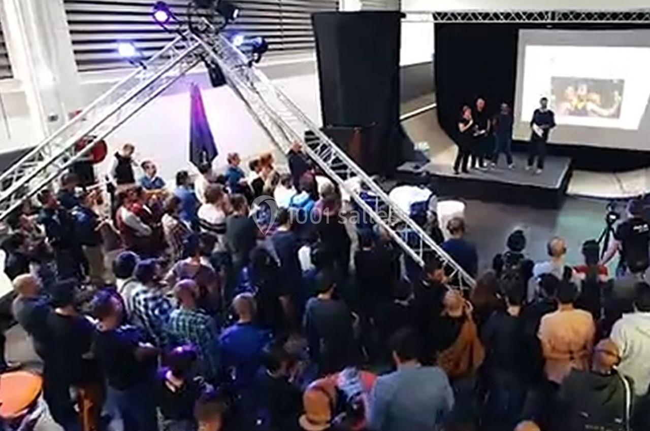 Un groupe de personnes assiste à une présentation sur scène dans un espace intérieur avec un écran projeté.