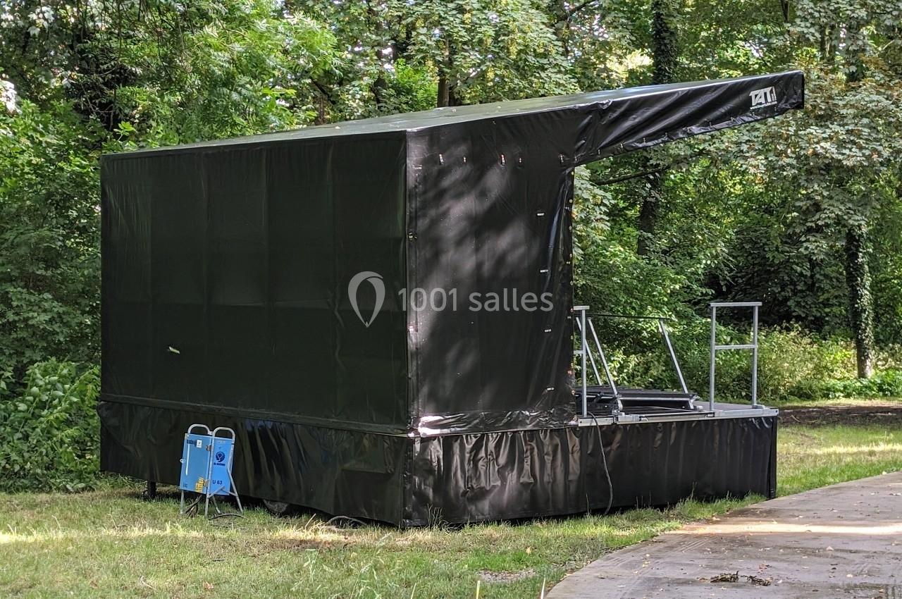 Scène mobile noire installée dans un espace extérieur verdoyant, entourée d'arbres et de végétation.