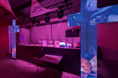 Miniature Equinoxe #196 Un bus stationné de nuit devant un bâtiment illuminé, avec des passants en arrière-plan.