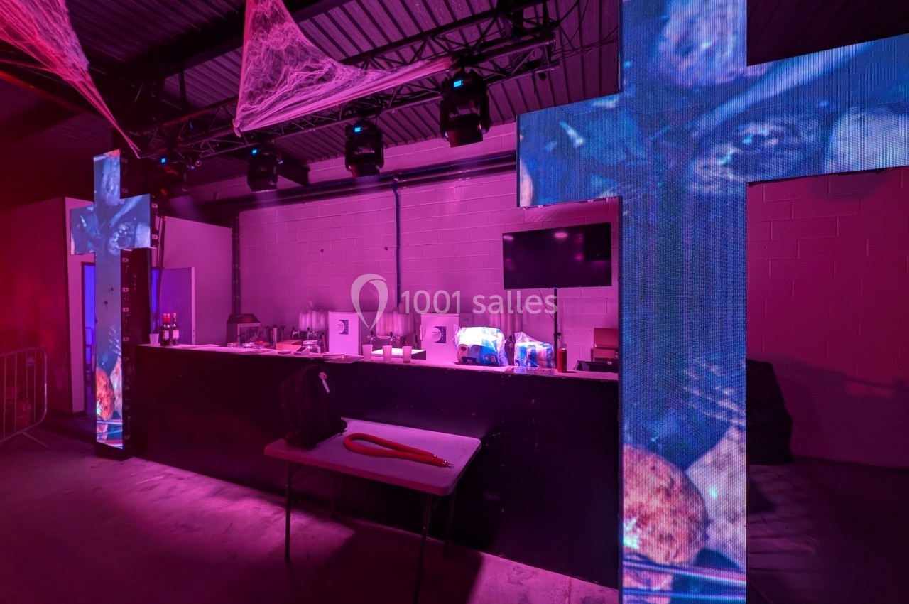 Salle décorée pour un événement, éclairée de lumières roses avec des croix lumineuses et une table au premier plan.