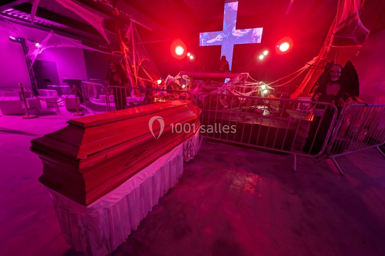 Cercueil en bois dans une ambiance sombre et lumineuse, décorée de toiles d'araignée et éclairée par des lumières rouges.