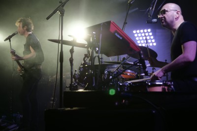 Un bus stationné de nuit devant un bâtiment illuminé, avec des passants en arrière-plan.