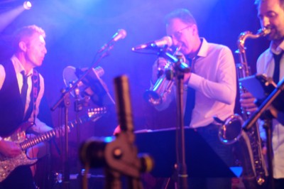 Un bus stationné de nuit devant un bâtiment illuminé, avec des passants en arrière-plan.